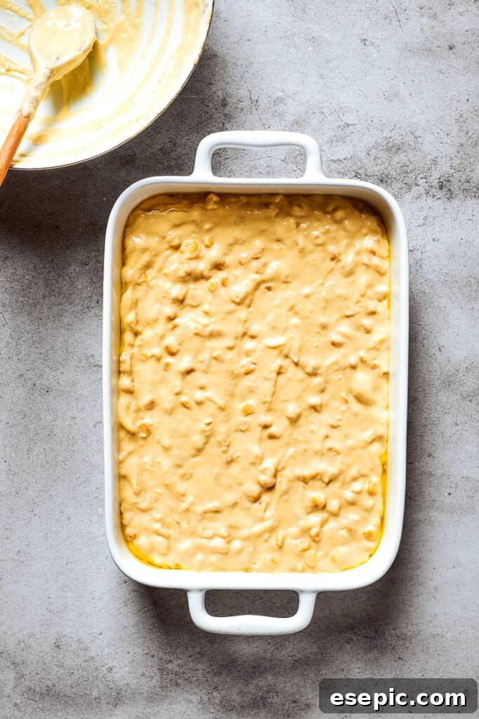 Smooth corn souffle batter is shown evenly spread in a white baking pan, ready for the oven.