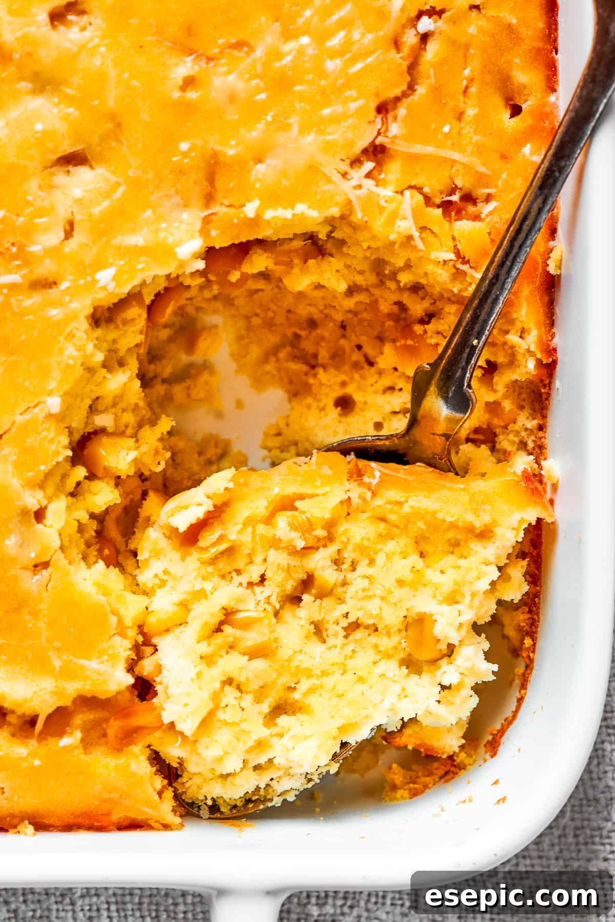 A close-up image of a spoon taking out a large, creamy bite of corn souffle, highlighting its inviting texture.