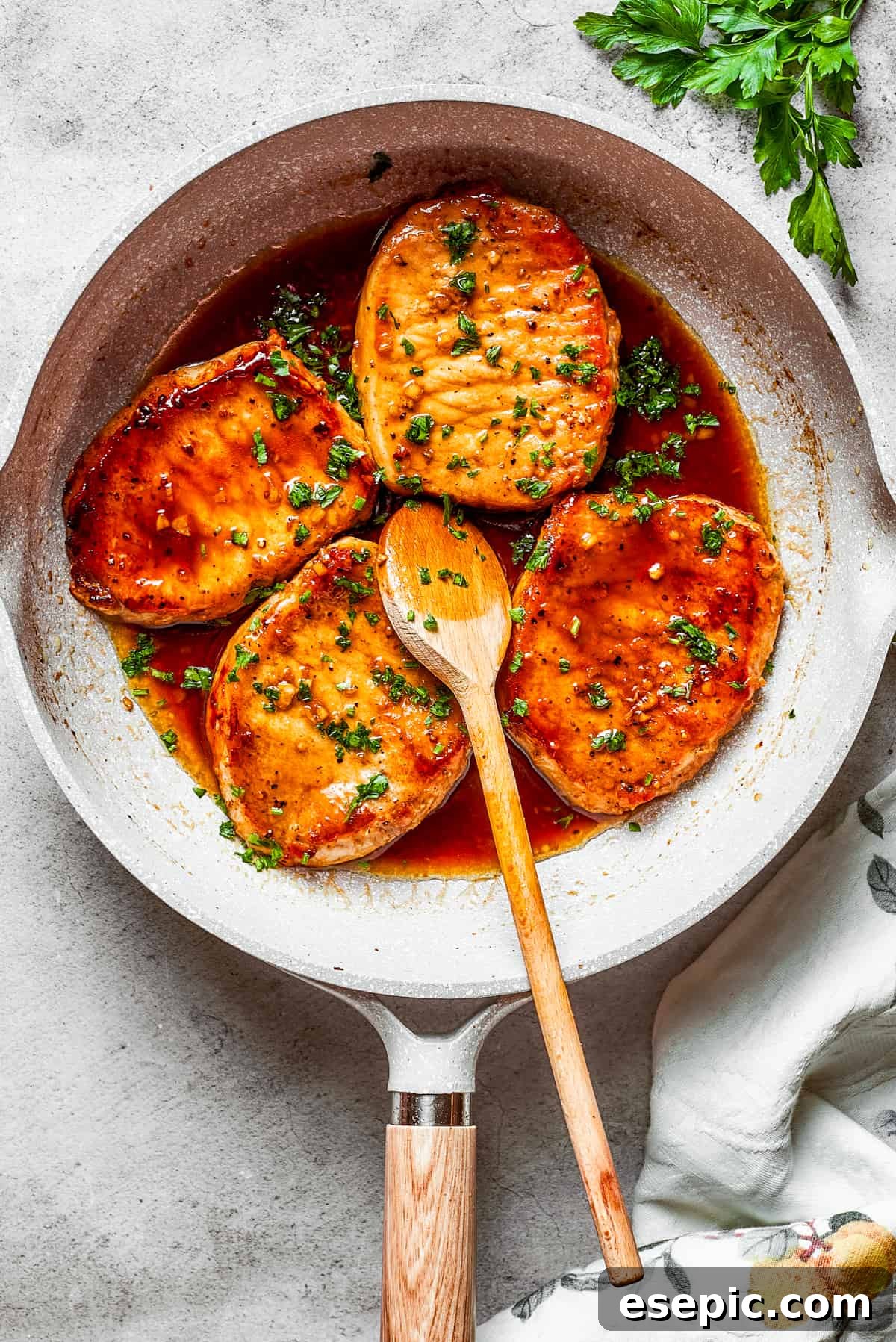 These Honey Garlic Pork Chops are the perfect blend of sweet-salty with a punch of extra flavor from minced garlic. Ready in 20 minutes! Four honey garlic pork chops cooking in a skillet with a wooden spoon stirring through.