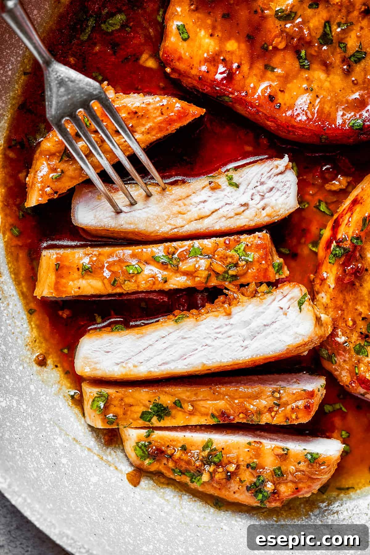 These Honey Garlic Pork Chops are the perfect blend of sweet-salty with a punch of extra flavor from minced garlic. Ready in 20 minutes! Sliced pork chops with a fork reaching for a piece.