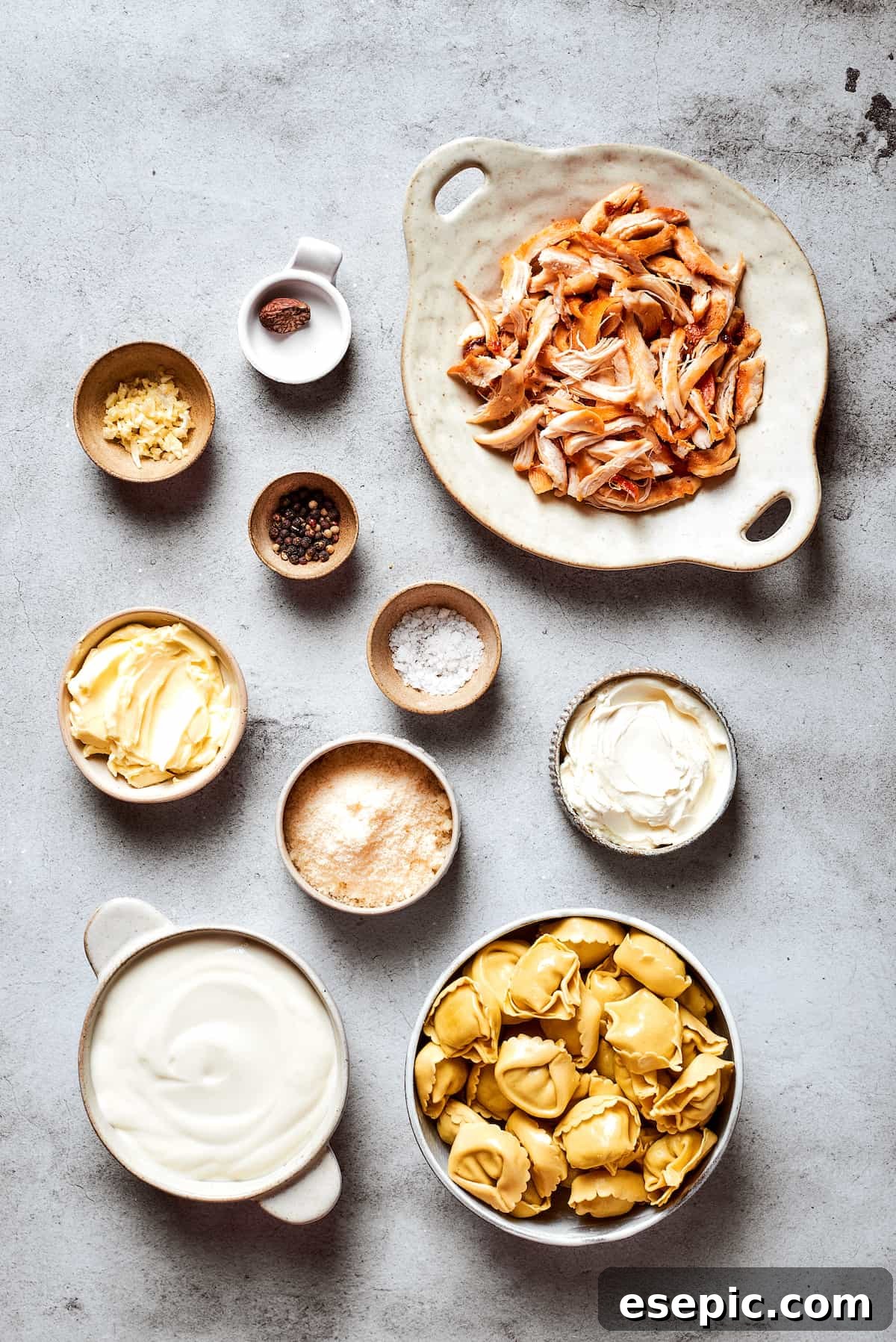 The organized ingredients for making chicken tortellini alfredo: cooked chicken, cheese tortellini, butter, garlic, heavy cream, cream cheese, nutmeg, Parmesan, salt, pepper, basil, and parsley.