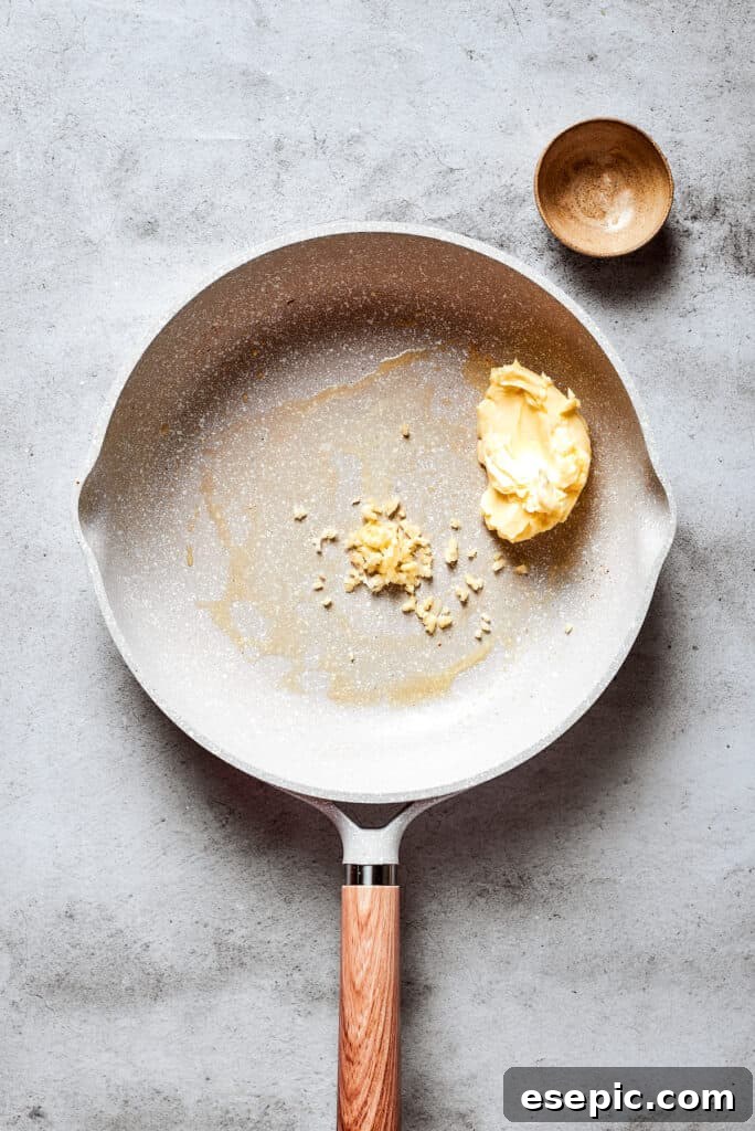 A white skillet holds melted butter and finely chopped garlic, beginning the sauce preparation.