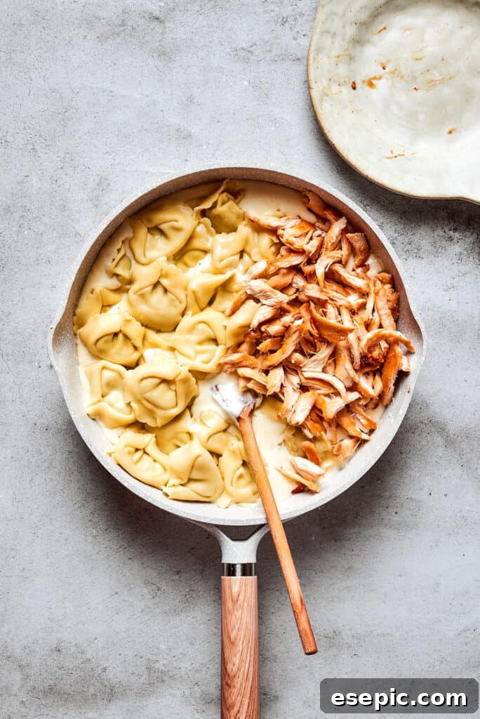 Cheese tortellini and shredded rotisserie chicken are gently stirred into the rich cream cheese Alfredo sauce in a white skillet.