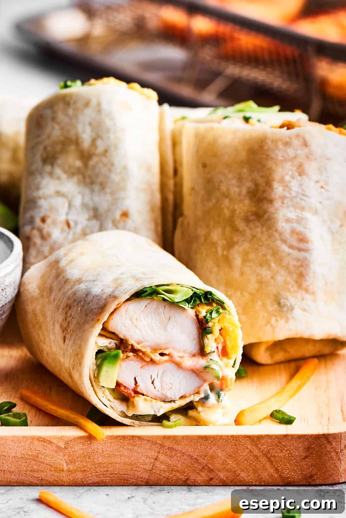 Perfectly sliced Buffalo Chicken Wraps arranged on a rustic wooden cutting board, with a small bowl of creamy Ranch dressing for dipping.
