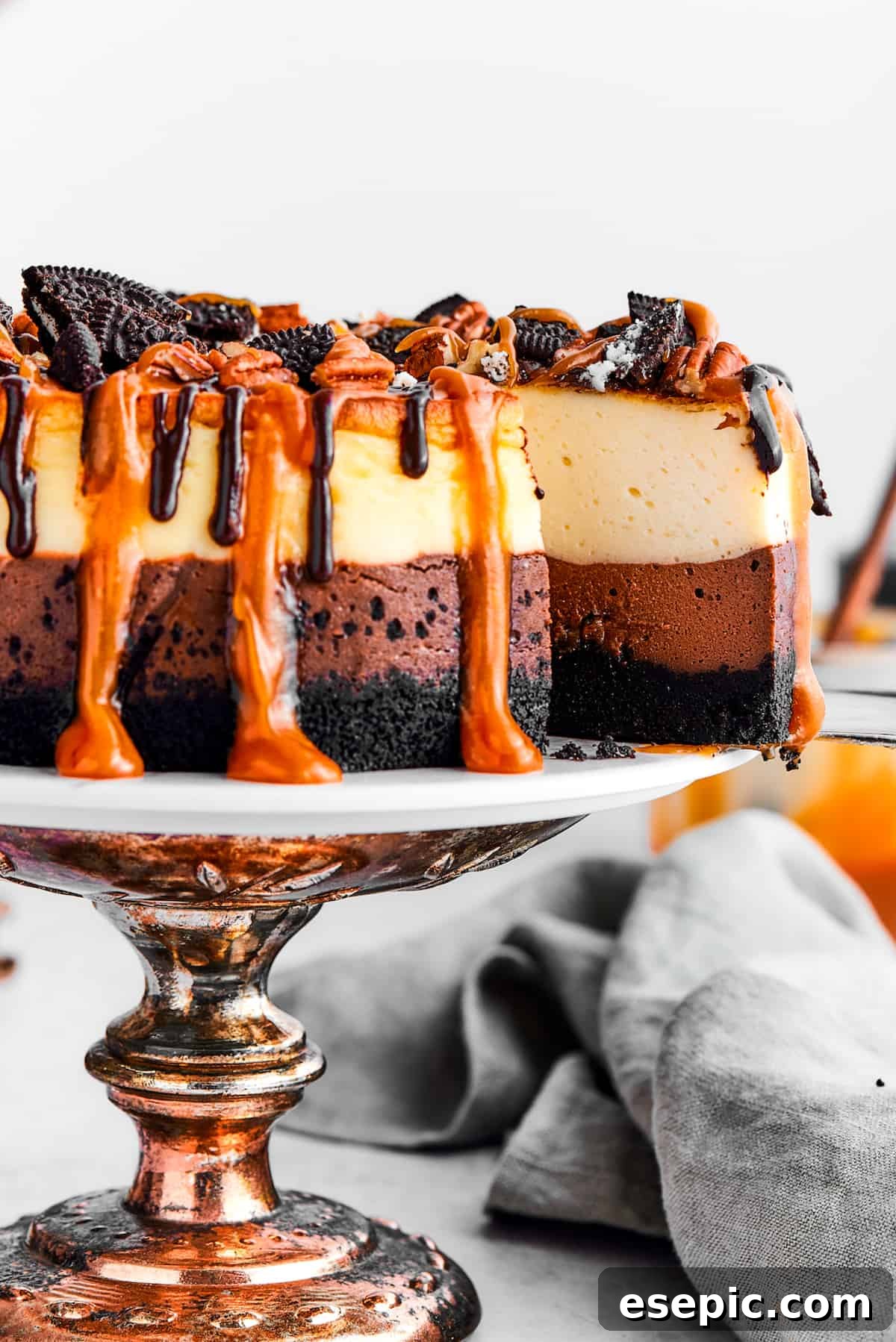 A slice of turtle cheesecake is slightly pulled out of the whole cheesecake on the cake stand.