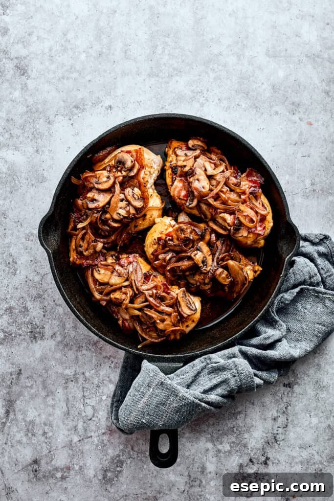 Four mushroom-topped chicken breasts in a cast iron skillet.