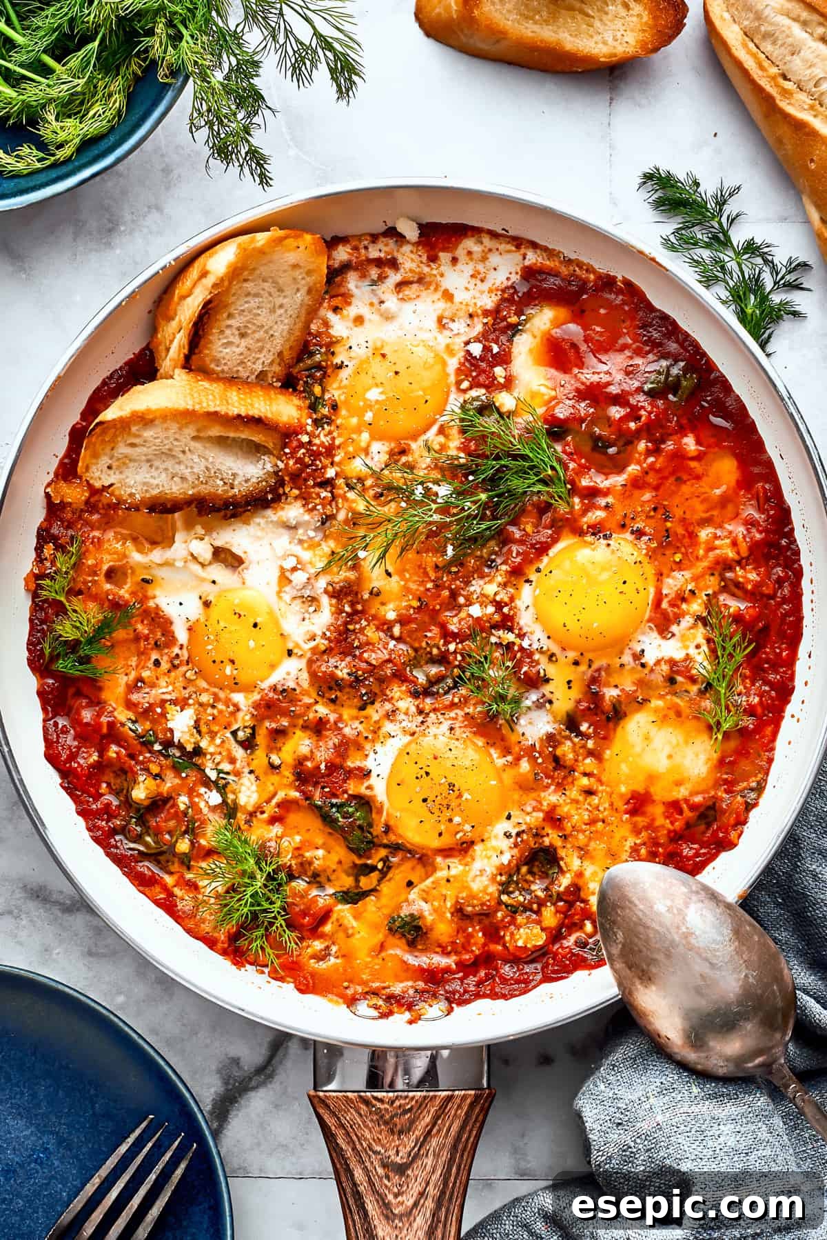 Cooked eggs in purgatory in a skillet are garnished with parsley and toasted bread with a silver spoon resting on its edge.