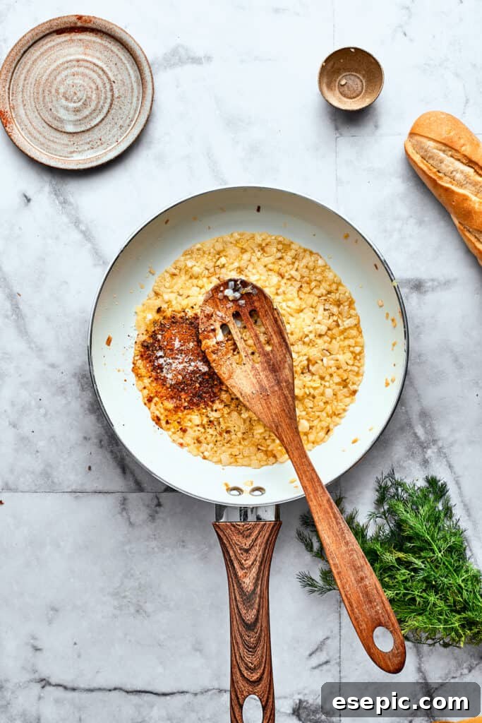 A wooden spoon stirs diced tomatoes into a skillet of onion and garlic.