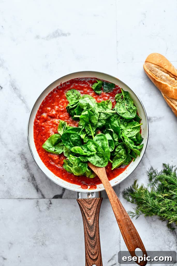 Bright green spinach leaves are stirred into a skillet of homemade tomato sauce.