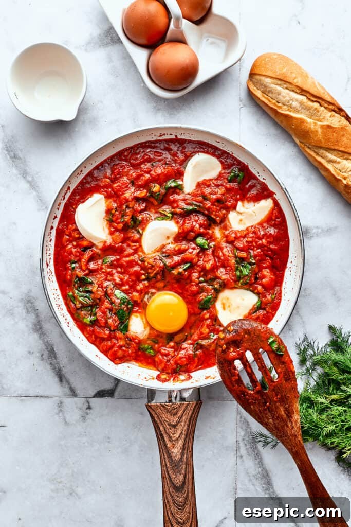 Eggs are added to a skillet of tomato sauce, spinach, and cheese.