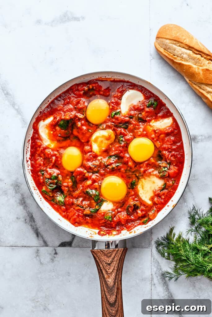 A skillet of eggs in purgatory shows white slices of mozzarella and yellow egg yolks in red sauce.