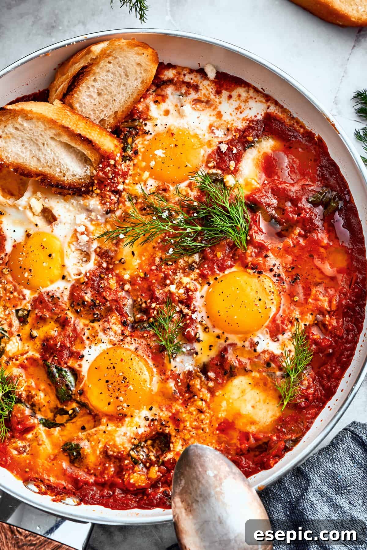 Overhead up close image of a skillet with cooked eggs in purgatory and garnished with parsley and toasted bread.