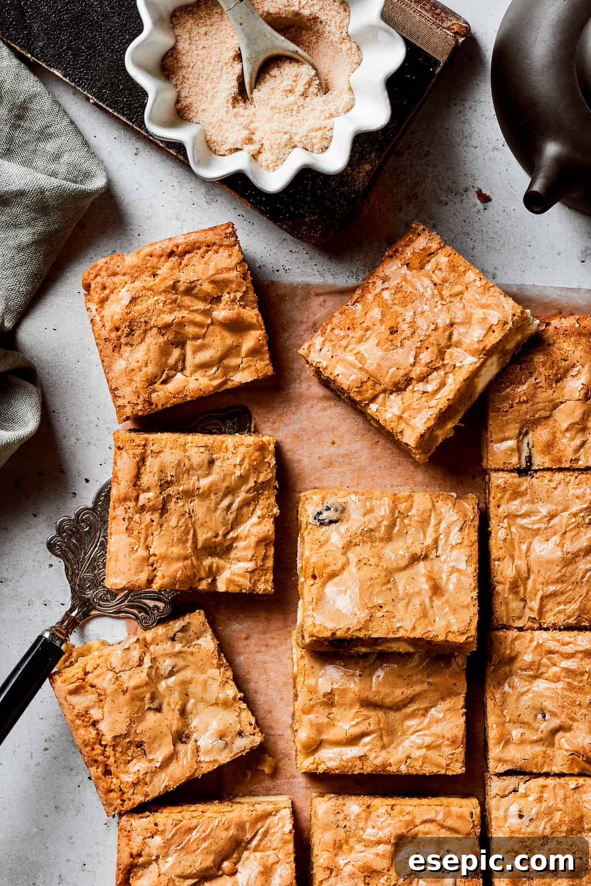 A cutting board of golden blonde brownie squares, each studded with white chocolate chips and pecans, with a bowl of brown sugar nearby. The brownies are perfectly baked, with a slightly crinkled top and a soft, chewy interior.