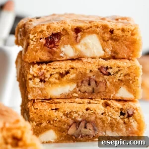 A stack of three blonde brownies, showing visible white chocolate chips and pecans, indicating a rich and flavorful treat.