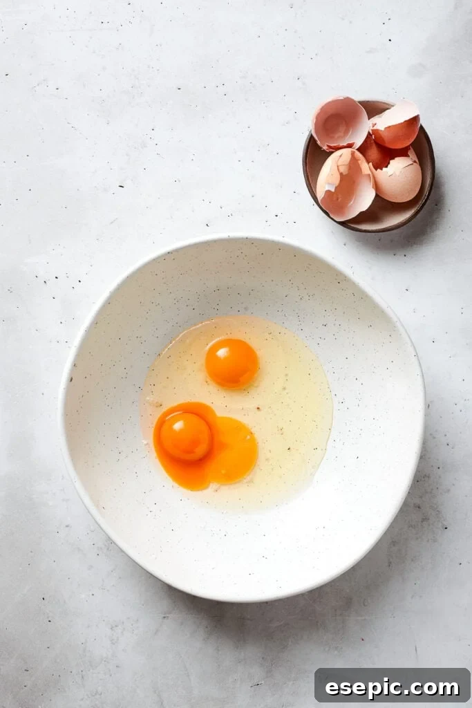 Two whole eggs and a separate egg yolk are shown in a pristine white bowl, ready to be incorporated into the blonde brownie batter.