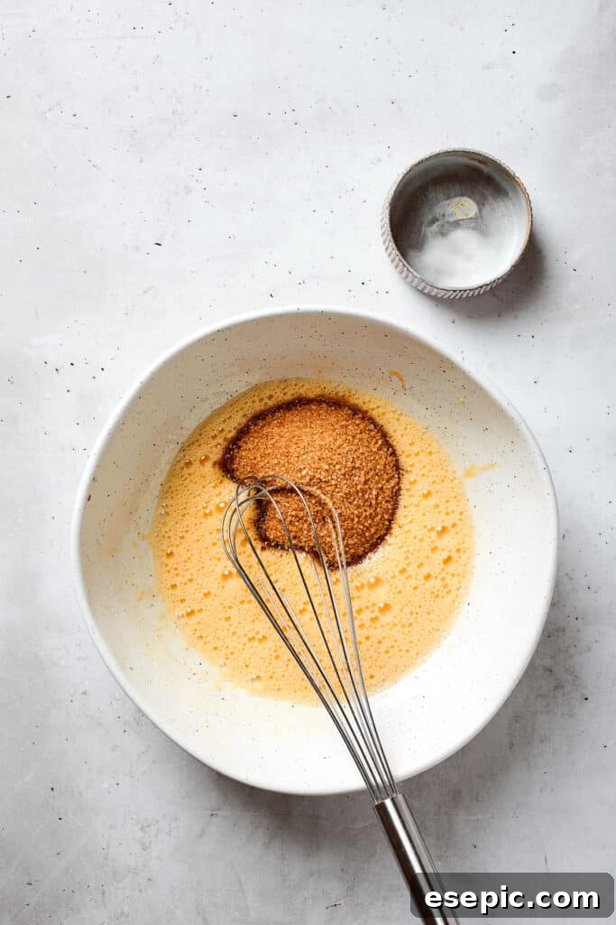 Golden brown sugar is being gently poured into a bowl containing whisked eggs, a crucial step in building the rich base for blonde brownies.