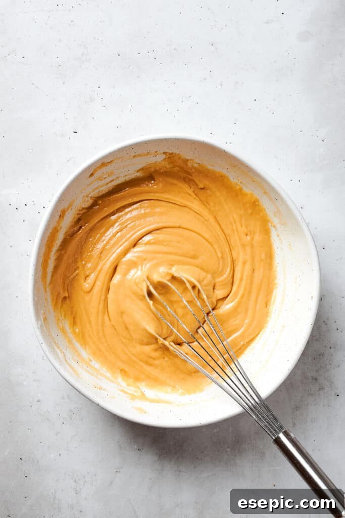 A whisk is gently used to incorporate the dry ingredients into the wet blonde brownie batter, mixing until just combined to prevent overworking the gluten.