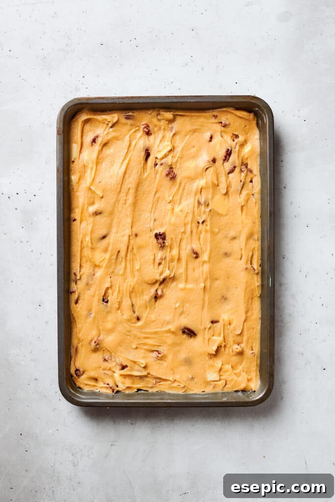 The smooth, thick blonde brownies batter is being carefully spread into a prepared 9x13-inch baking pan, ready for the oven.