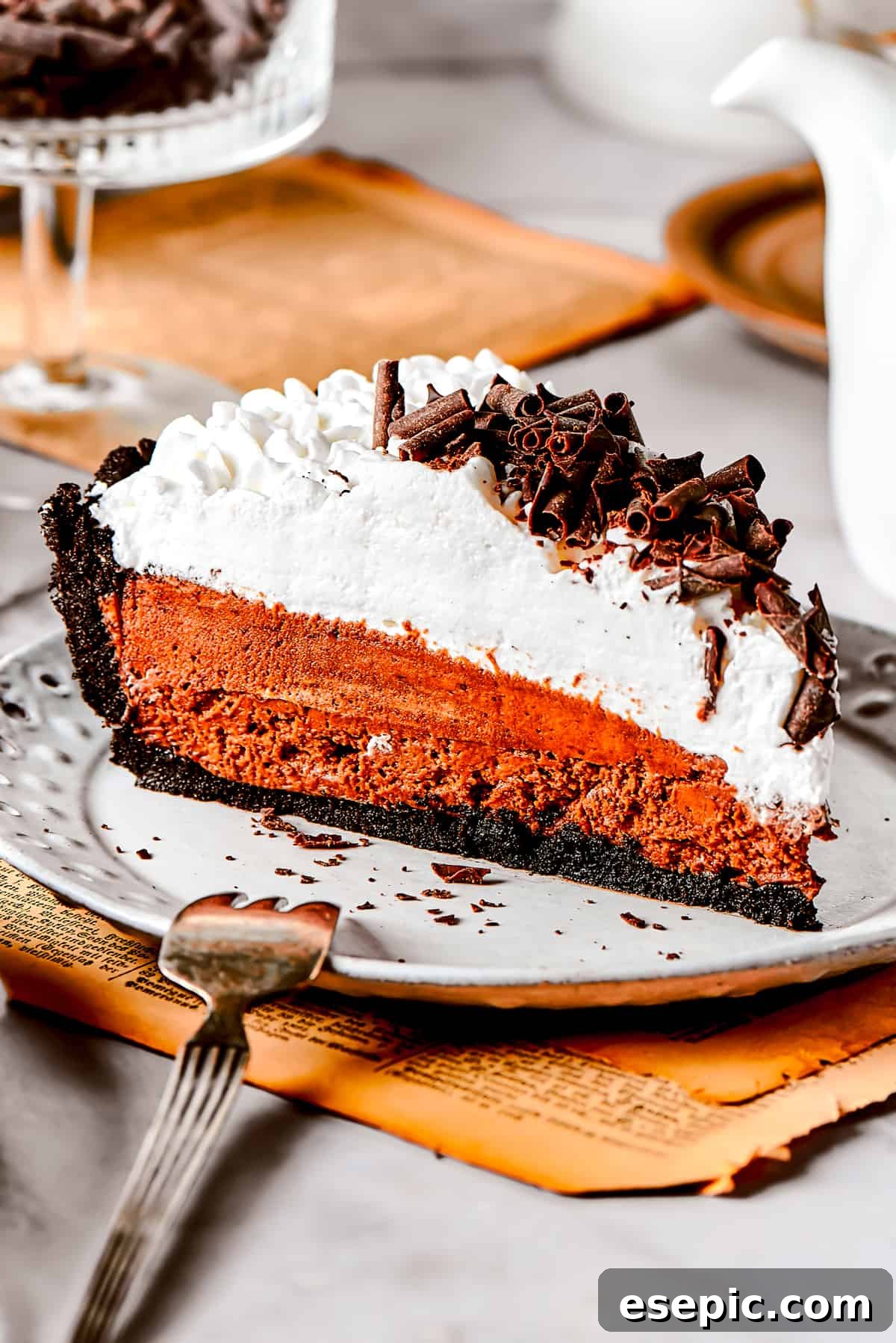 A perfect slice of French Silk Pie, ready to be enjoyed. Slice of French silk pie served on a dessert plate, showcasing its distinct layers of dark chocolate filling and light whipped cream.