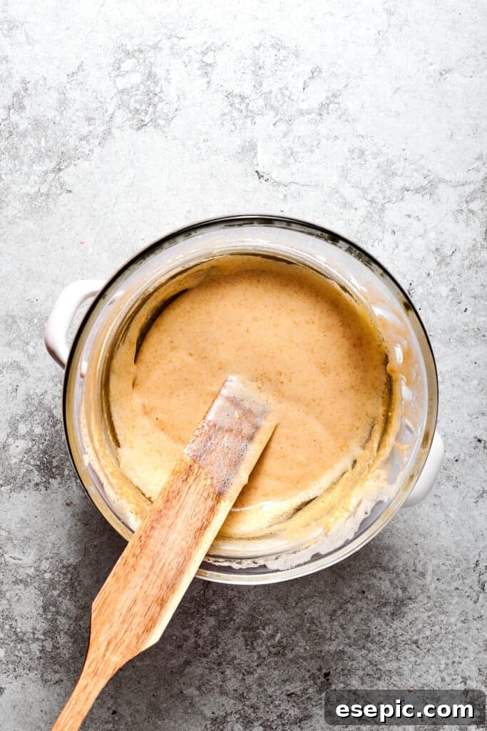 Gently cooking the egg mixture over simmering water. A spatula gently stirs the egg, sugar, and water mixture in a bowl set over simmering water, illustrating the double boiler method.