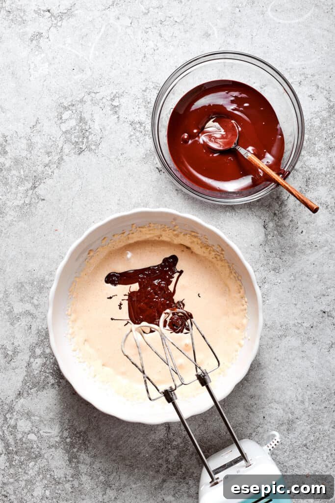 Combining the melted chocolate with the egg mixture. The cooled, beaten egg mixture is combined with the slightly cooled melted chocolate in a bowl, being beaten until fully integrated.