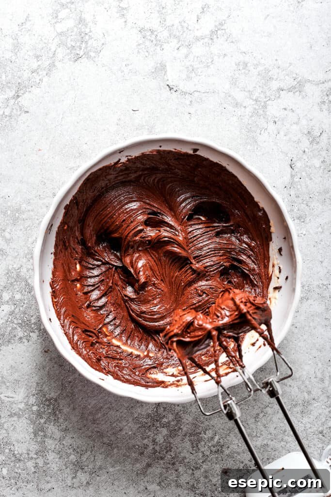 Ensuring the chocolate and egg mixture is perfectly smooth. A close-up of the chocolate and egg mixture being beaten with an electric mixer, forming a smooth and uniform consistency.
