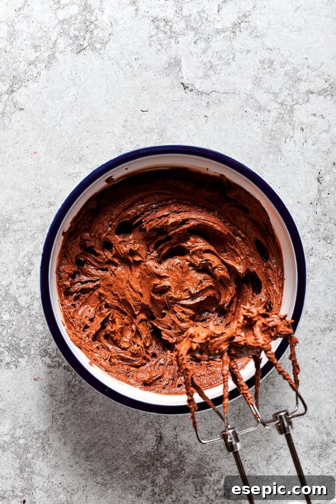 Gradually adding the chocolate mixture to the whipped butter. Small portions of the chocolate-egg mixture are gradually beaten into the whipped butter until fully incorporated.