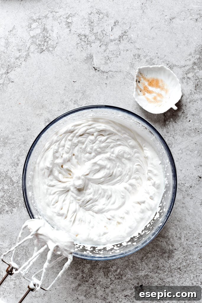 Freshly whipped cream ready for the pie topping. A bowl of freshly whipped heavy cream with the beaters from an electric mixer resting above it, ready for topping the pie.