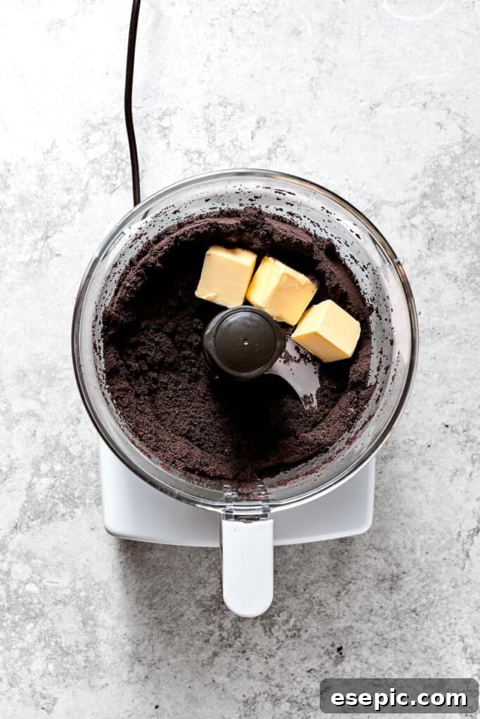 Starting the Oreo crust: Oreos and butter in the food processor. Oreo cookies and cubes of unsalted butter are placed in a food processor, ready to be blended for the pie crust.
