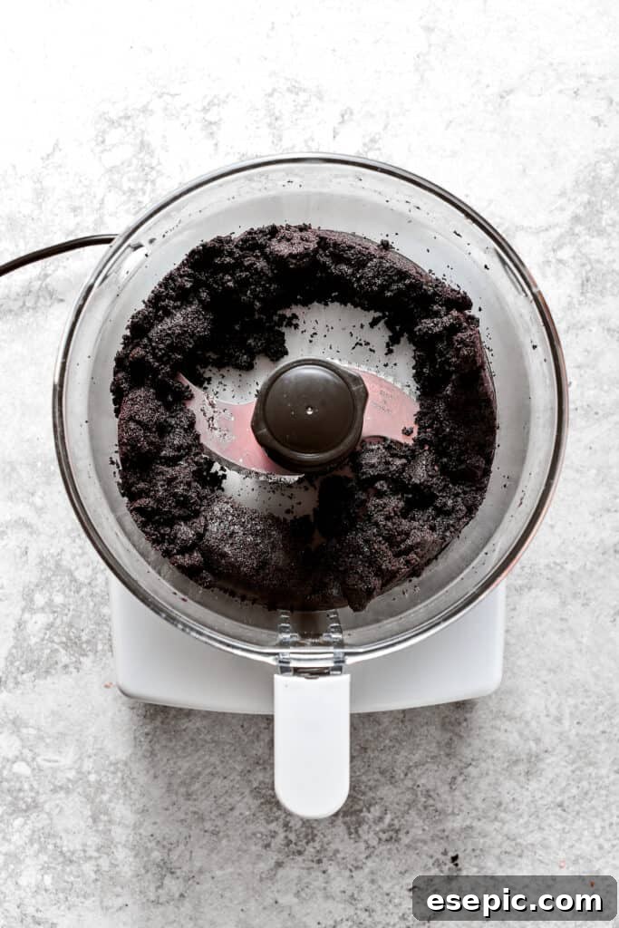 Processing the Oreo cookie and butter mixture. The food processor is actively blending the Oreo cookies and butter into fine crumbs for the pie crust.