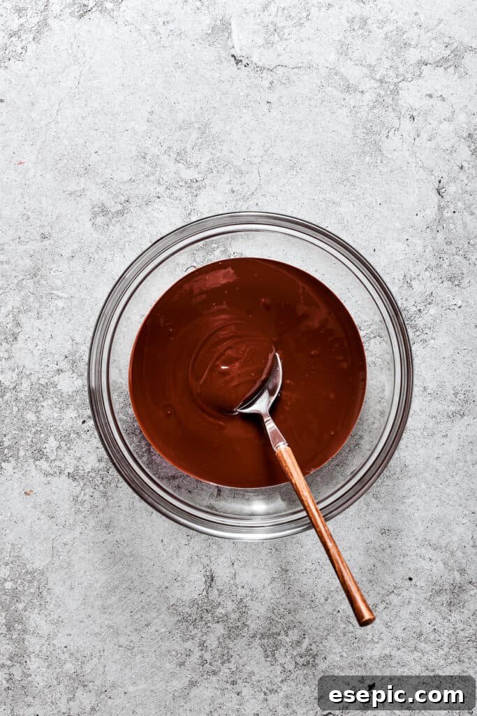 Melting the chocolate for the silky filling. Finely chopped bittersweet chocolate melted in a glass bowl over a double boiler, stirred with a wooden spoon until smooth.