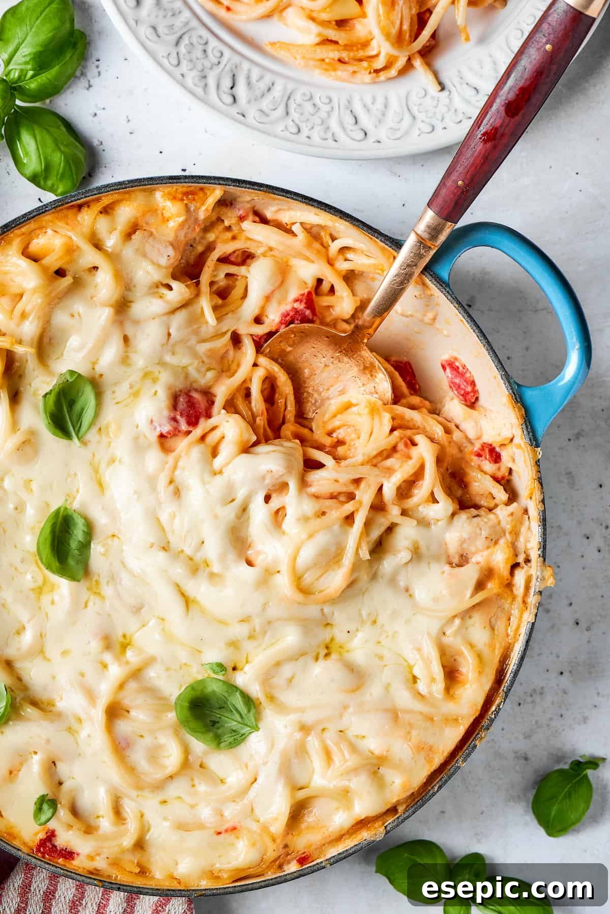 Basil garnish on hot cheesy chicken spaghetti Fresh basil garnishes a pot of cheesy chicken spaghetti, with a serving spoon ready to dish out.