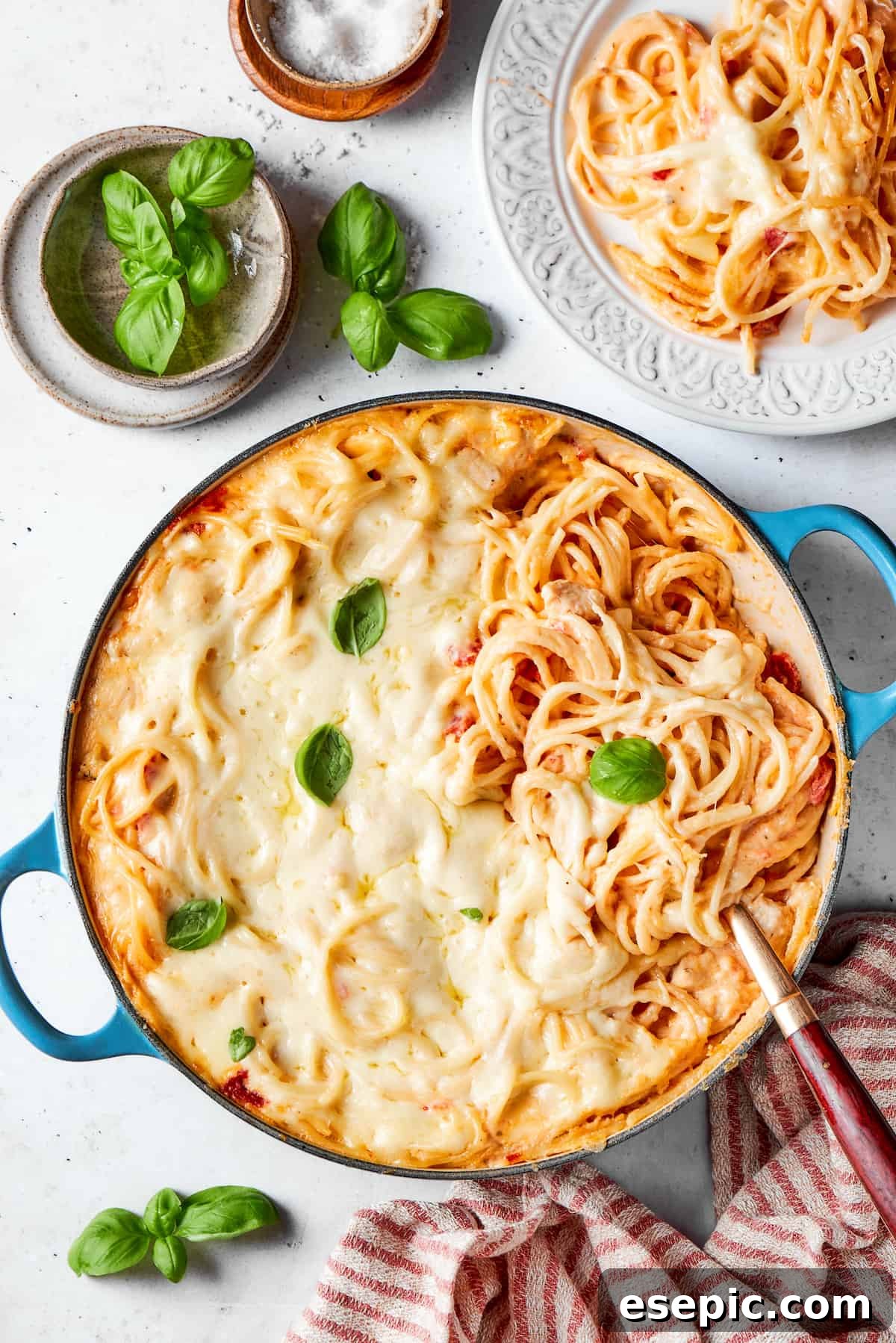 Delicious Cheesy Chicken Spaghetti with fresh basil A pot of cheesy chicken spaghetti on a table with a bowl of fresh basil leaves next to it, ready for garnish.