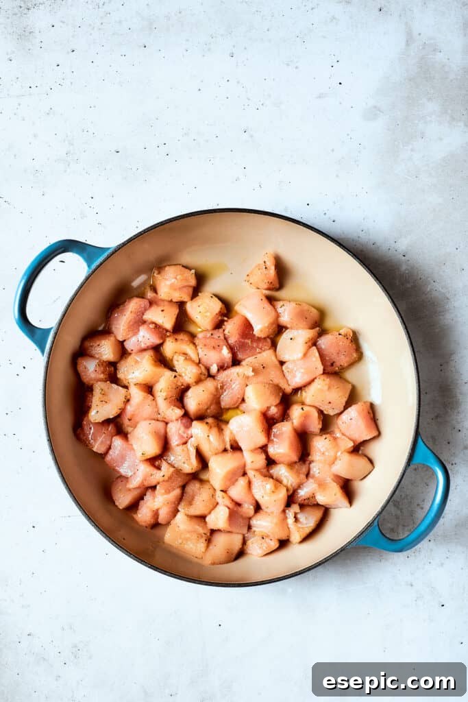 Searing chicken for cheesy spaghetti Pieces of seasoned chicken cook and brown in a pot, releasing savory aromas.