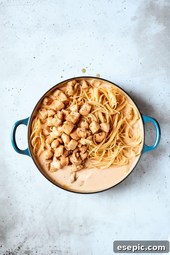 Combining chicken and pasta with the creamy sauce The cooked chicken and spaghetti are being added to the creamy sauce in a large pot.