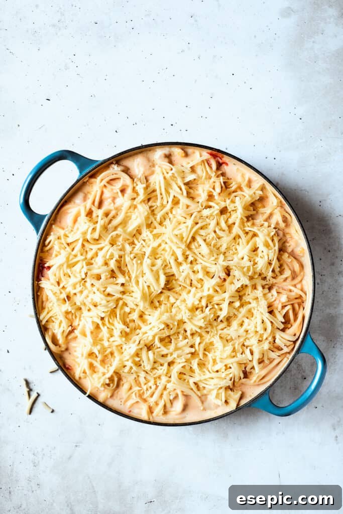 Topping the chicken spaghetti with mozzarella cheese Shredded mozzarella cheese is generously scattered over the pot of pasta and chicken mixture before baking.