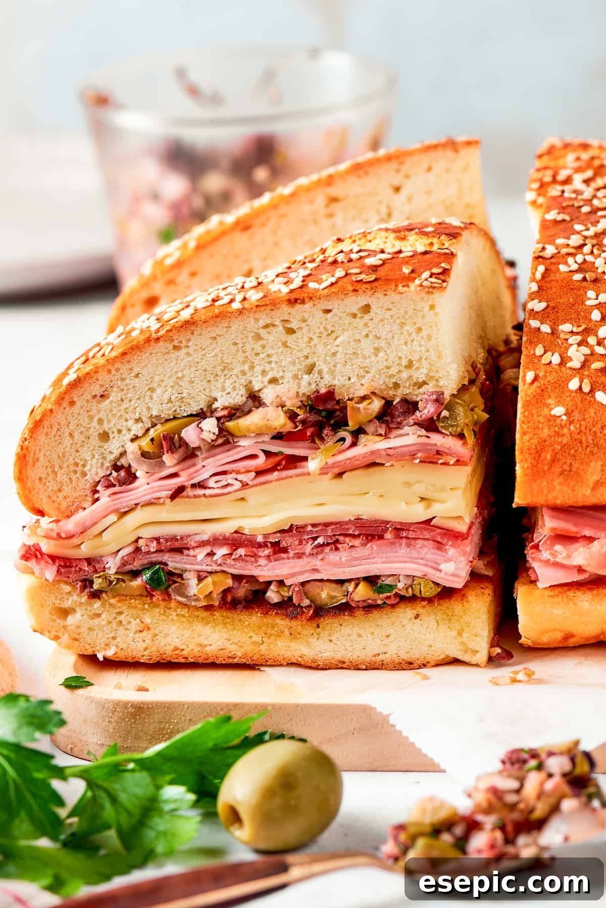 Two generously thick slices of muffaletta sandwich, showcasing the vibrant layers of olive salad, deli meats, and cheeses, are presented on a wooden cutting board.