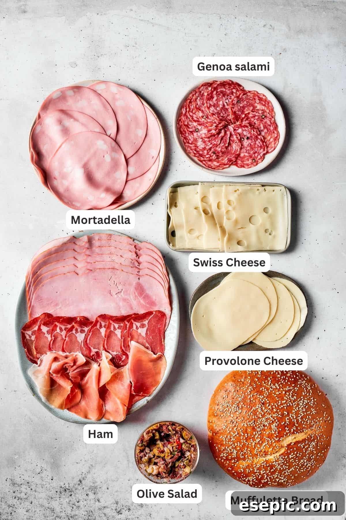 A selection of premium Italian deli meats and cheeses for a Muffaletta sandwich, including mortadella, capicola ham, Genoa salami, provolone cheese, Swiss cheese, and prosciutto di Parma, alongside the vibrant homemade olive salad.