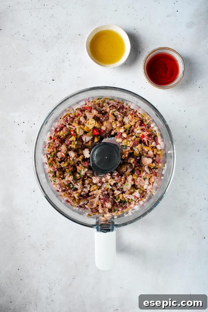 The olive salad is finely blended in a food processor, creating a coarse, flavorful mixture ready for the muffaletta sandwich.