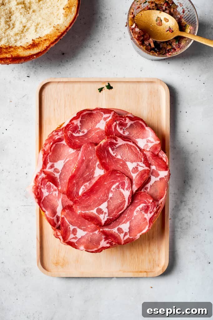 Thinly sliced deli ham is carefully placed on top of the other stacked meats, forming another layer of the delicious muffaletta sandwich.