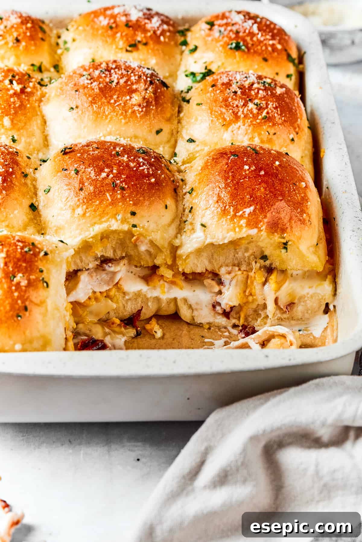 Chicken sliders in a baking dish with two of the sliders exposed to show the savory chicken, bacon, and cheese mixture inside.