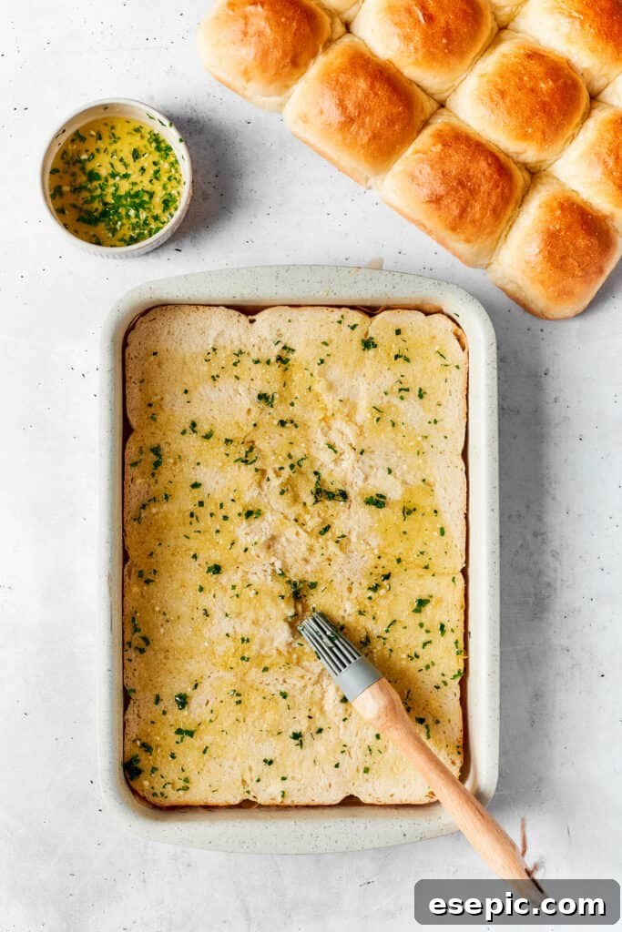 A melted butter mixture being added to the bottom halves of Hawaiian rolls in a baking dish.