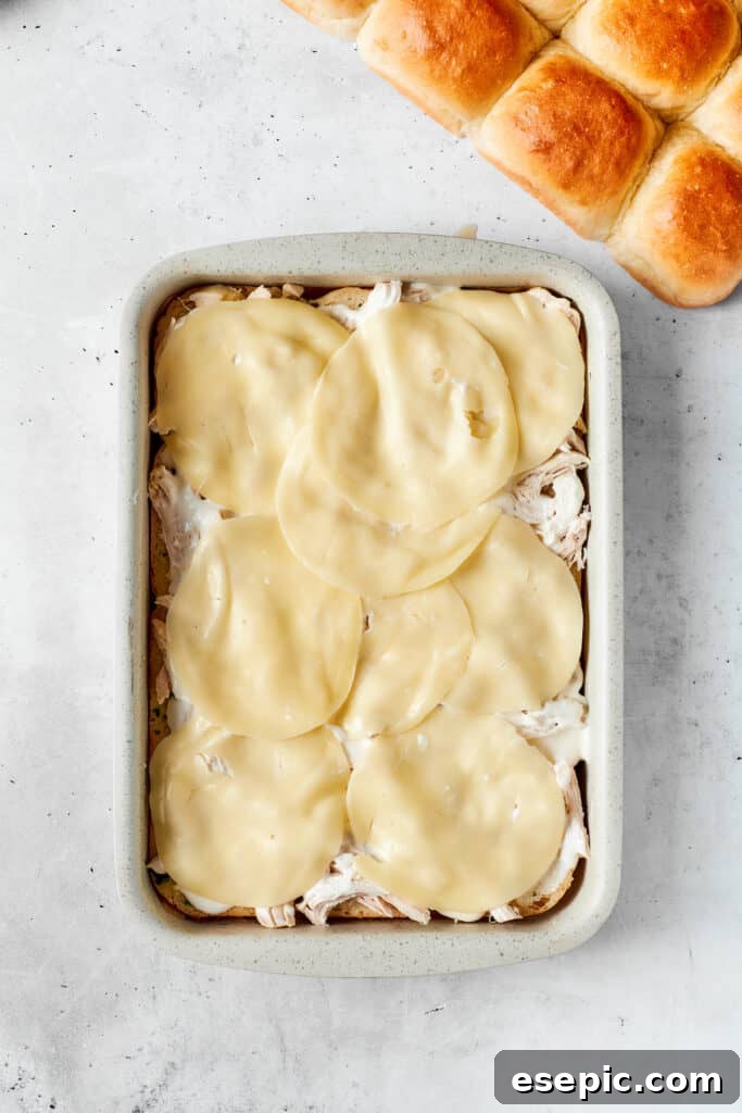 Slices of Provolone cheese being carefully placed over the chicken and bacon layers.