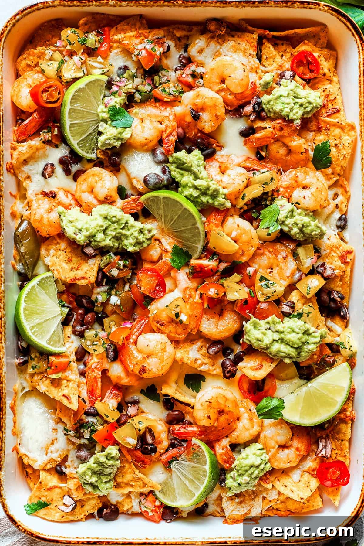 Nacho chips topped with shrimp, cheese, black beans, tomatoes, and a garnish of guacamole and slices of lime.