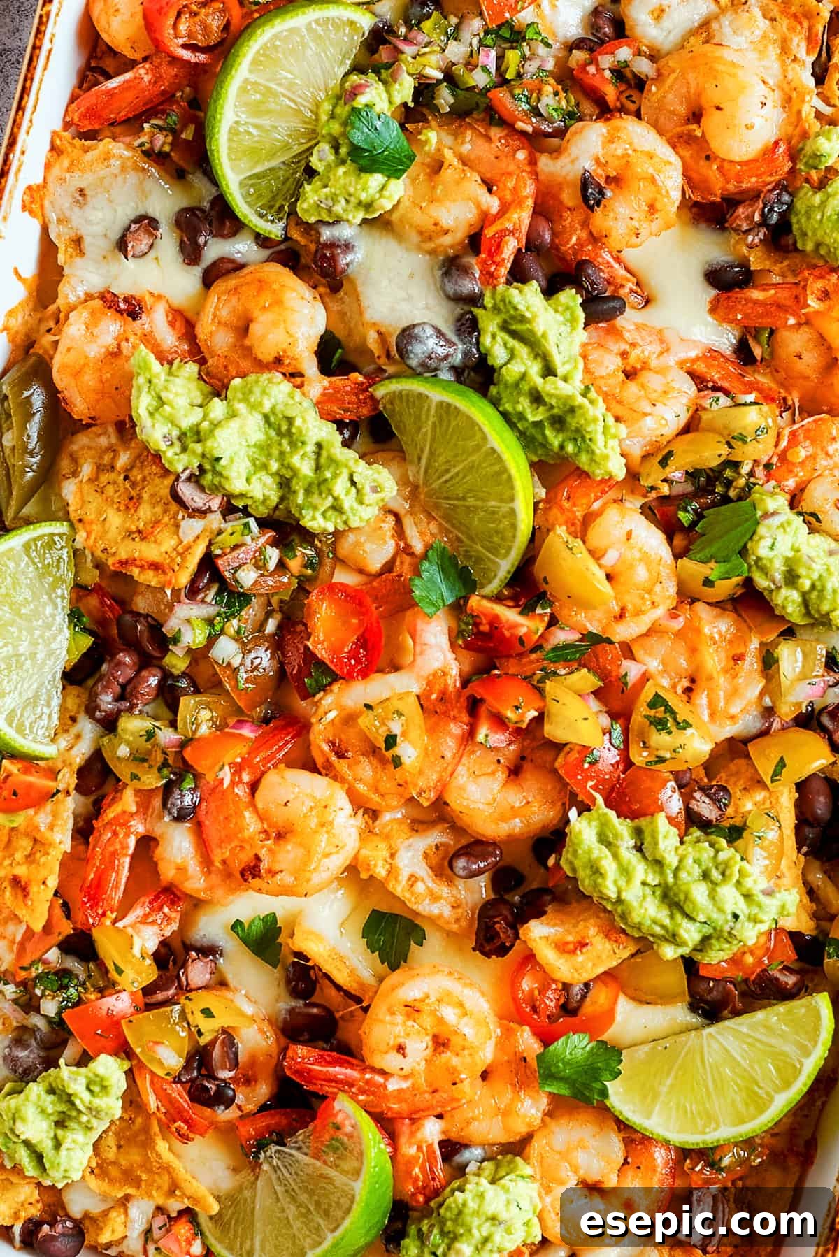 Tortilla chips topped with shrimp, cheese, black beans, tomatoes, and a garnish of guacamole and slices of lime.
