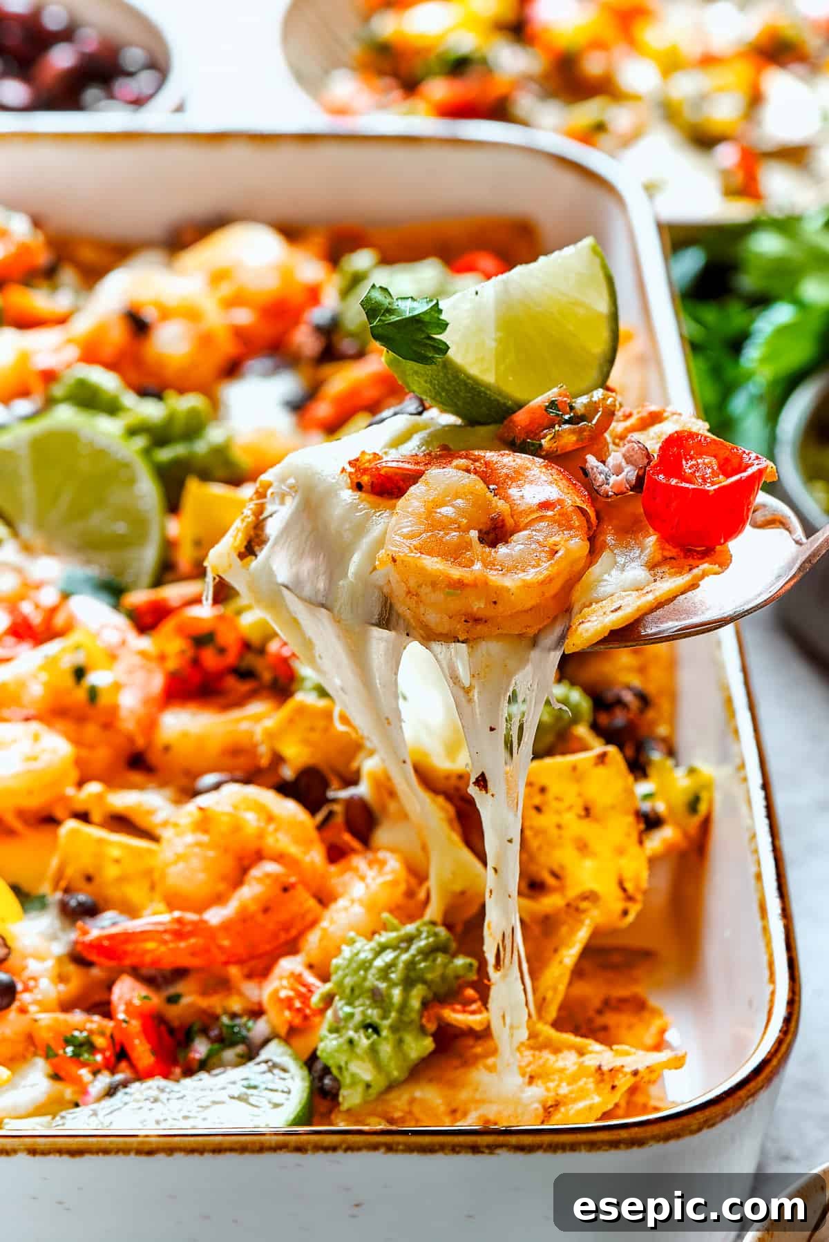 A spoon lifts out a cheesy portion of shrimp nachos.