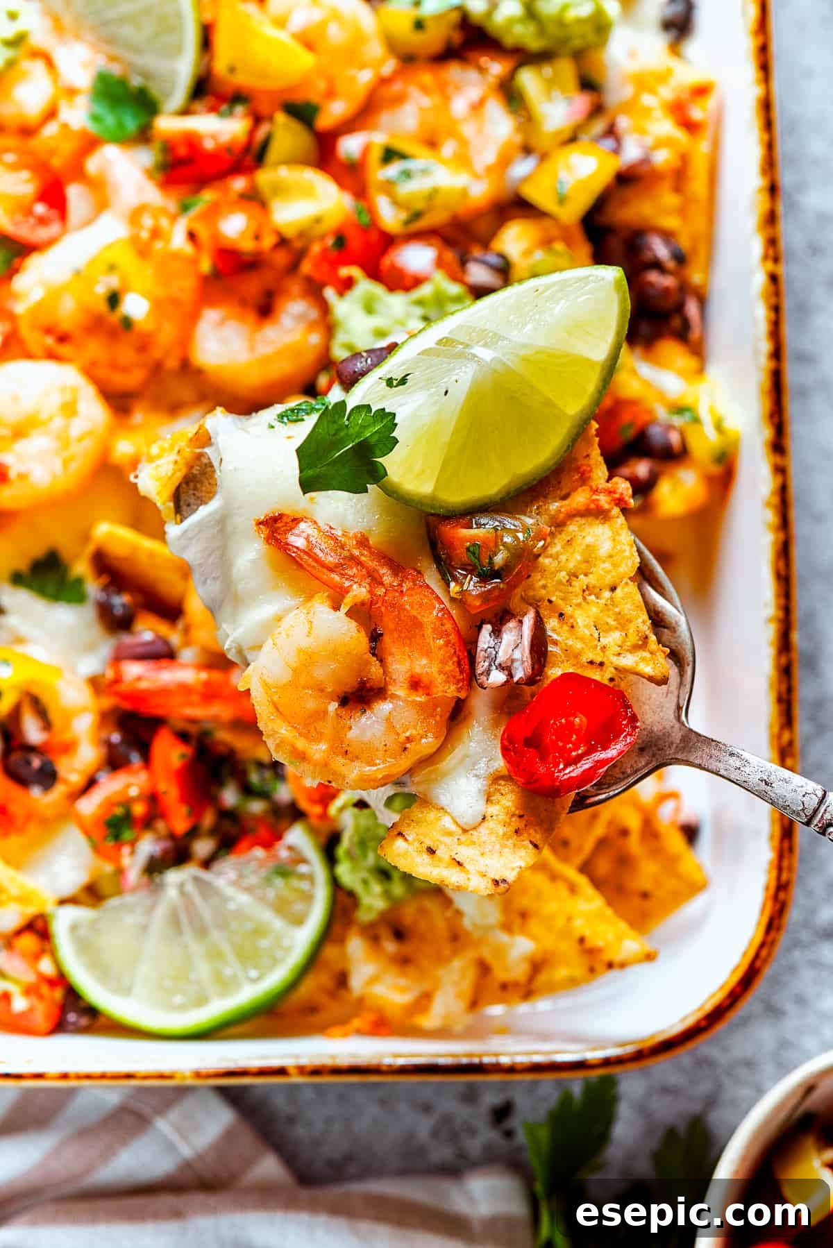 A spoon lifts out nachos from a baking dish.