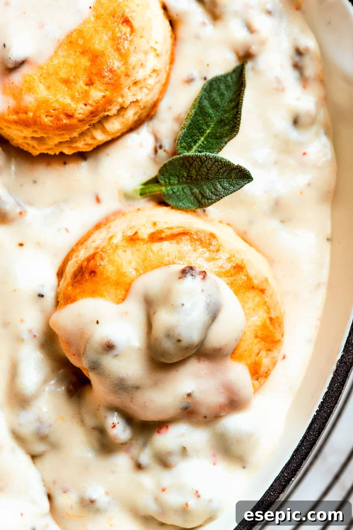 Close-up image of biscuits topped with generous amounts of creamy sausage gravy, garnished with fresh herbs.