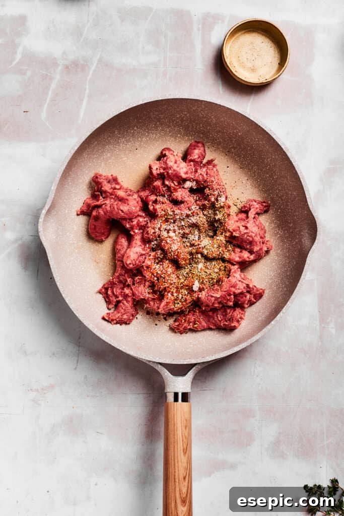Breakfast sausage and herbs are added to a hot skillet, ready to be browned.