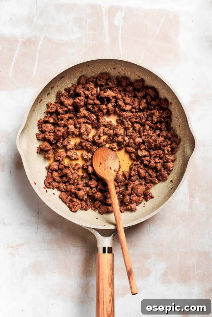 A wooden spoon stirs the crumbled breakfast sausage in the pan, ensuring even browning.